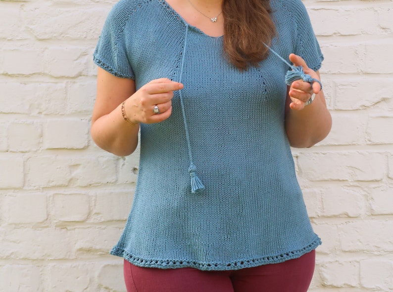 Pu&ograve; includere: Un top in maglia blu chiaro con maniche corte e scollo a V. Il top presenta un cordino con nappa e un orlo decorativo. Il top &egrave; realizzato in morbido materiale a maglia. Il top &egrave; lungo circa 61 cm.