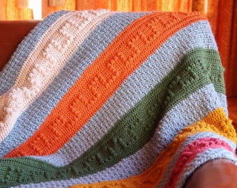 May include: A multi-colored crocheted blanket with stripes of pink, orange, green, yellow, and red. The blanket is folded and draped over a brown leather chair.