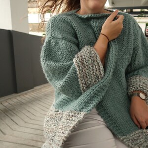 May include: A teal blue knitted cardigan with a white and brown patterned trim on the sleeves and hem.