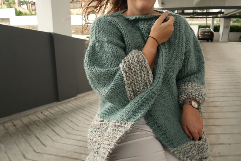 May include: A teal blue knitted cardigan with a white and brown patterned trim on the sleeves and hem.