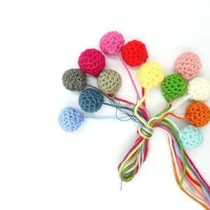K&ouml;nnte beinhalten: Eine Sammlung bunter geh&auml;kelter Kugeln mit langen Schn&uuml;ren. Die Kugeln sind in verschiedenen Farbt&ouml;nen von Rosa, Rot, Gr&uuml;n, Gelb, Blau, Orange und Grau.