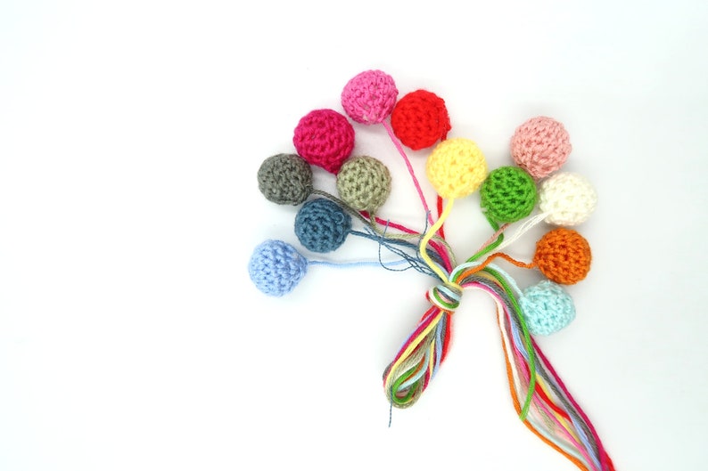 K&ouml;nnte beinhalten: Eine Sammlung bunter geh&auml;kelter Kugeln mit langen Schn&uuml;ren. Die Kugeln sind in verschiedenen Farbt&ouml;nen von Rosa, Rot, Gr&uuml;n, Gelb, Blau, Orange und Grau.