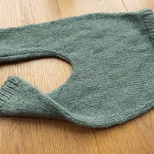 May include: A soft, green knitted baby romper with a leg opening on one side.