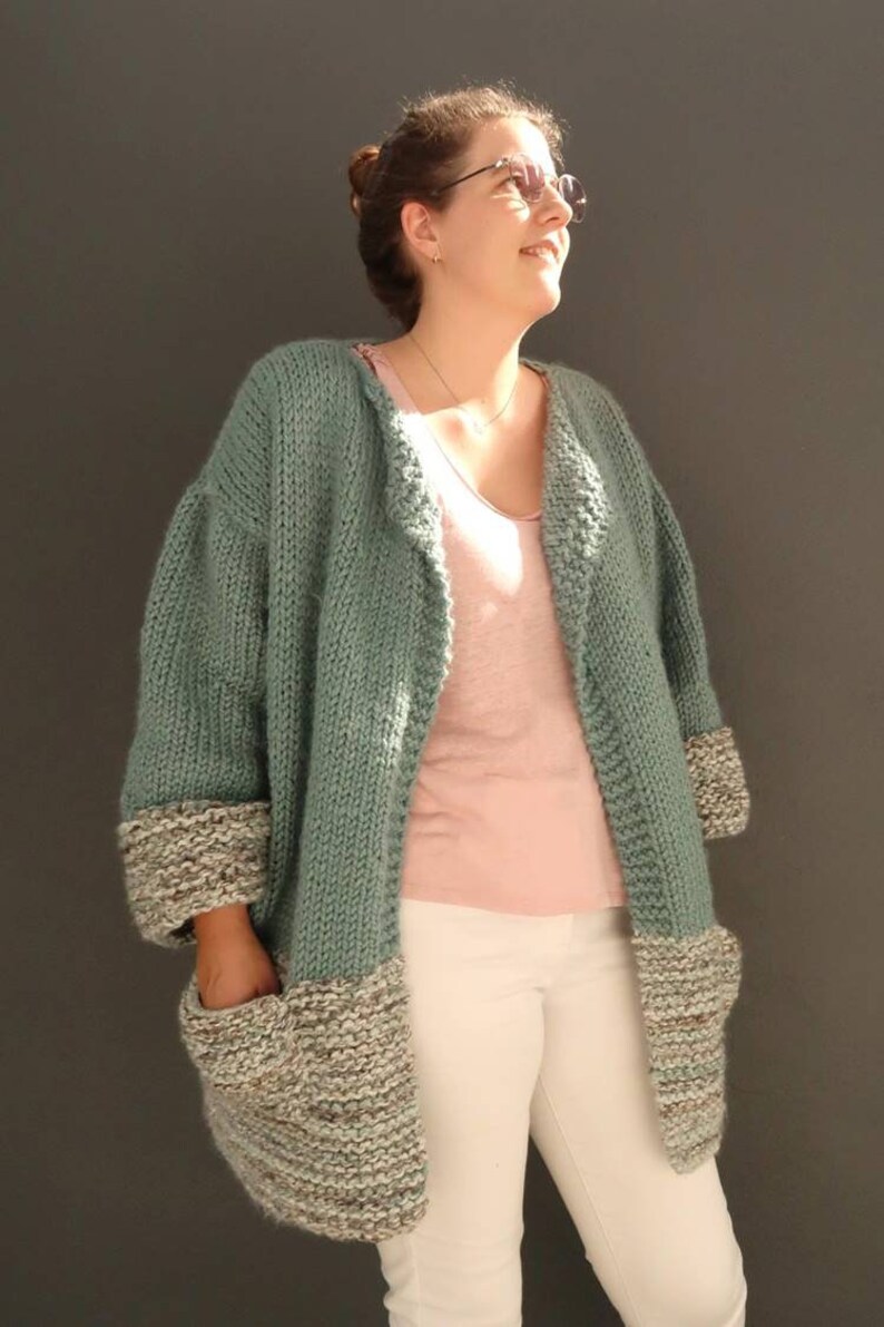 May include: A teal knitted cardigan with brown and white trim on the sleeves and pockets. The cardigan is open in the front and has a relaxed fit.