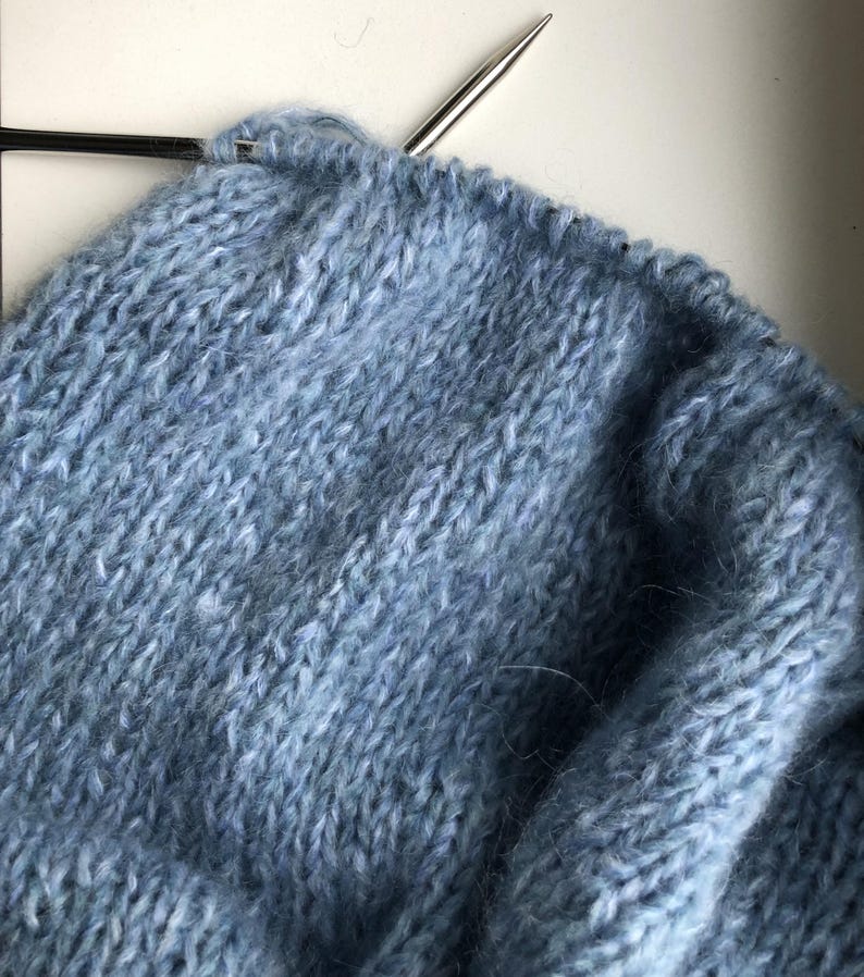May include: Close-up of a blue knitted fabric with a knitting needle in the top left corner.