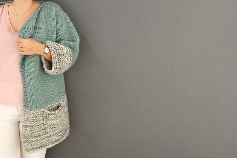 May include: A teal knitted cardigan with a brown and white striped bottom and cuffs. The cardigan has a pocket on the left side.