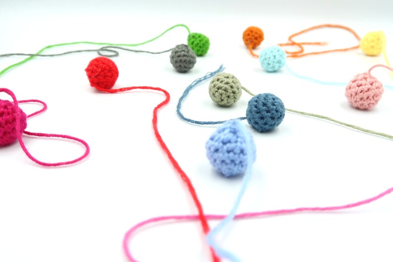 K&ouml;nnte beinhalten: Eine Sammlung bunter geh&auml;kelter Kugeln, die mit Garn aneinandergereiht sind. Die Kugeln sind in den Farben Rot, Rosa, Blau, Gr&uuml;n, Grau und Orange.