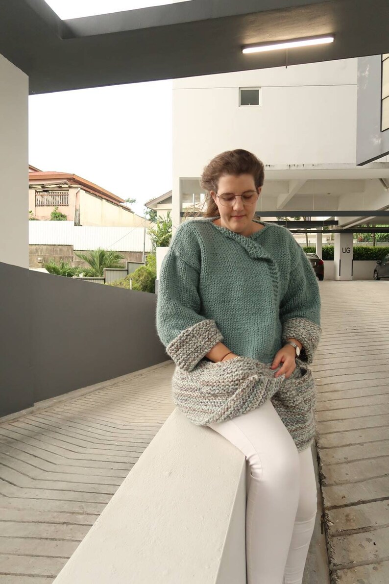 May include: A woman wearing a teal knitted sweater with a multi-colored knitted scarf and white pants.