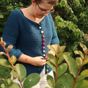 K&ouml;nnte beinhalten: Ein tealblauer Strickcardigan mit bunten Kn&ouml;pfen. Der Cardigan ist locker geschnitten und hat einen V-Ausschnitt.