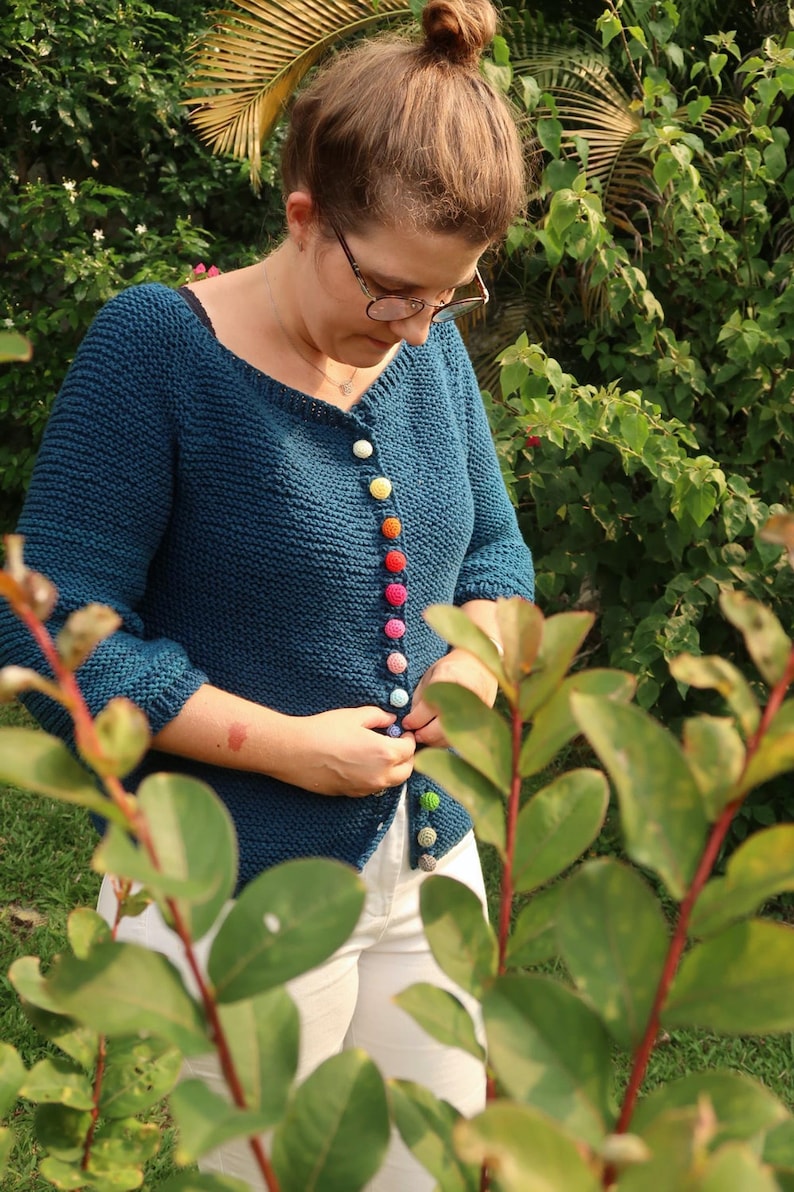 K&ouml;nnte beinhalten: Ein tealblauer Strickcardigan mit bunten Kn&ouml;pfen. Der Cardigan ist locker geschnitten und hat einen V-Ausschnitt.
