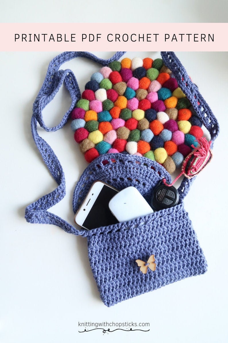May include: A crocheted blue crossbody bag with a colorful felt circle inside. The bag has a small wooden butterfly charm and is open to reveal a phone and keys.