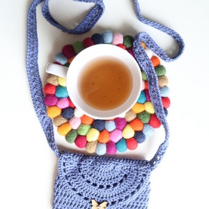 May include: A purple crocheted bag with a butterfly charm, a cup of tea, and a colorful felt coaster.