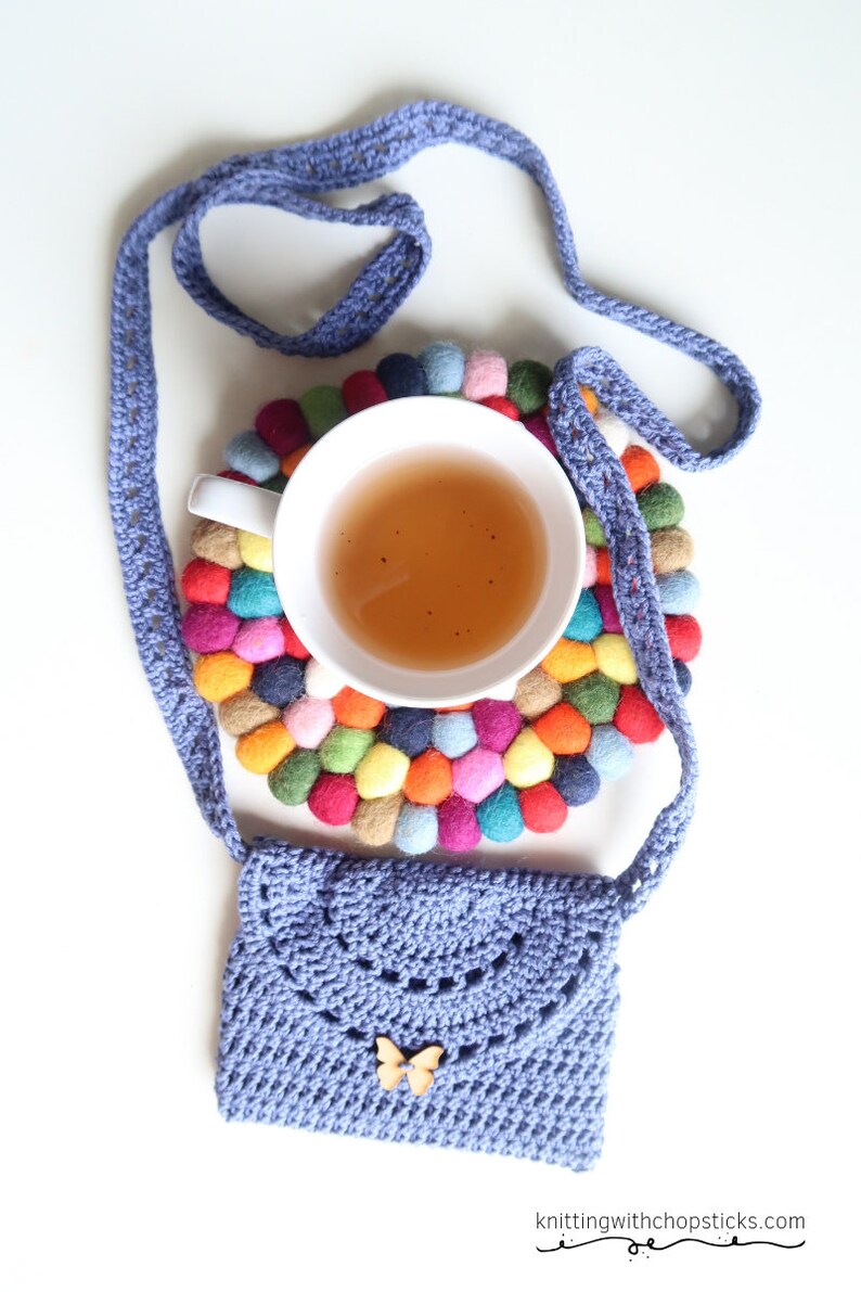 May include: A purple crocheted bag with a butterfly charm, a cup of tea, and a colorful felt coaster.