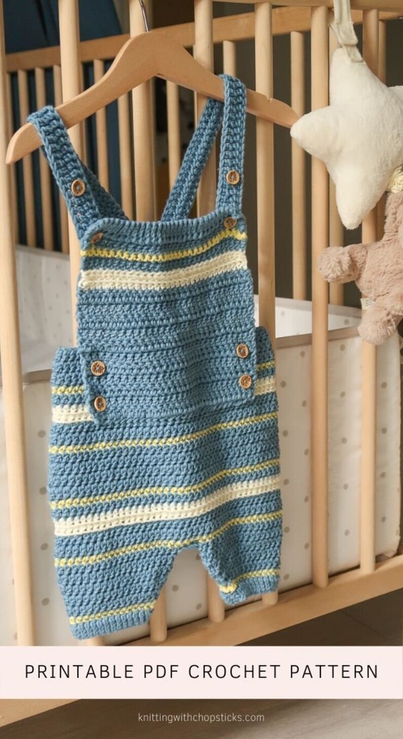 May include: A crochet baby romper with blue and white stripes and yellow accents. The romper has buttons on the straps and is hanging on a wooden hanger. The text "PRINTABLE PDF CROCHET PATTERN" is at the bottom of the image.