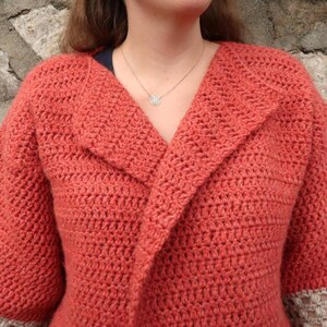 Peut inclure: Un cardigan en crochet avec un col ch&acirc;le de couleur orange br&ucirc;l&eacute;e. Le cardigan a une bordure en crochet de couleur beige clair sur les manches.