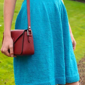 May include: A turquoise knitted dress with a white and black braided belt and a red leather crossbody bag.