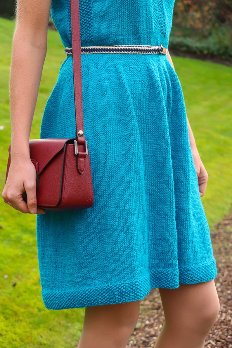 May include: A turquoise knitted dress with a white and black braided belt and a red leather crossbody bag.