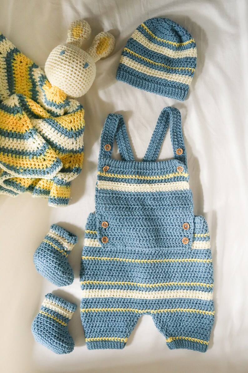 May include: A blue and white striped crocheted baby outfit with a matching hat and booties. The outfit includes a pair of overalls and a hat. The booties are also striped in blue and white.