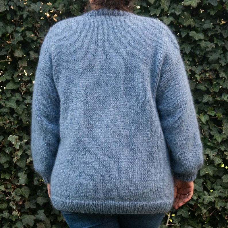 May include: A light blue knitted jumper with long sleeves and a crew neck.