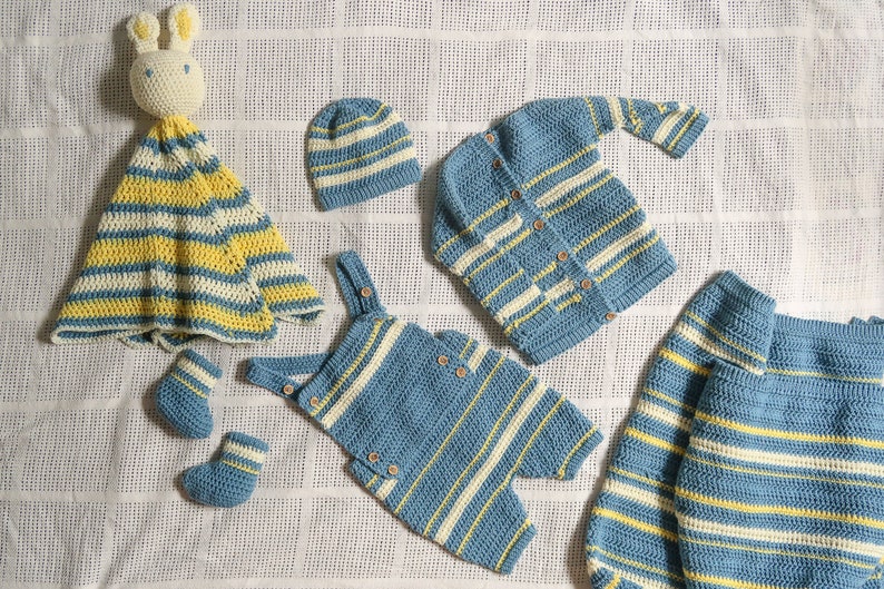 May include: A set of crocheted baby clothes in blue and yellow stripes. The set includes a hat, a cardigan, a pair of overalls, a pair of booties, and a crocheted blanket with a bunny head.