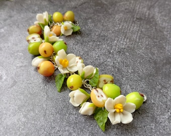May include: A handcrafted bracelet featuring miniature green and yellow fruit, white flowers with yellow centers, and green leaves. The bracelet is made of polymer clay and has a silver chain.