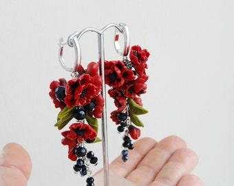 Può includere: Orecchini pendenti con grappoli di fiori rossi, foglie verdi e perline nere e blu. Gli orecchini sono sospesi ad anelli d'argento. Il design floreale è dettagliato, creando un accessorio unico.