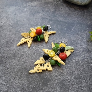 Peut inclure: Paire de boucles d'oreilles fantaisie avec des formes de fromage suisse, des olives, des tomates et des tranches de citron. Les boucles d'oreilles sont suspendues à des crochets argentés.