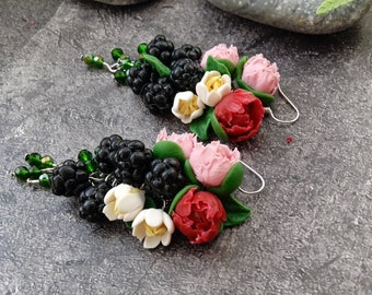 May include: A pair of handcrafted earrings featuring clusters of black berries, pink and red flowers, and white flowers. The earrings also have green beaded accents and silver-colored hooks. The floral and berry design is set against a gray background.