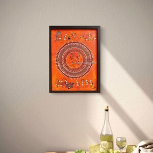 Pu&ograve; includere: Un dipinto rettangolare incorniciato su sfondo arancione con intricati disegni a linee bianche. L'opera mostra un grande motivo mandala circolare centrale circondato da piccole figure stilizzate, animali e scene di villaggio in stile tradizionale.