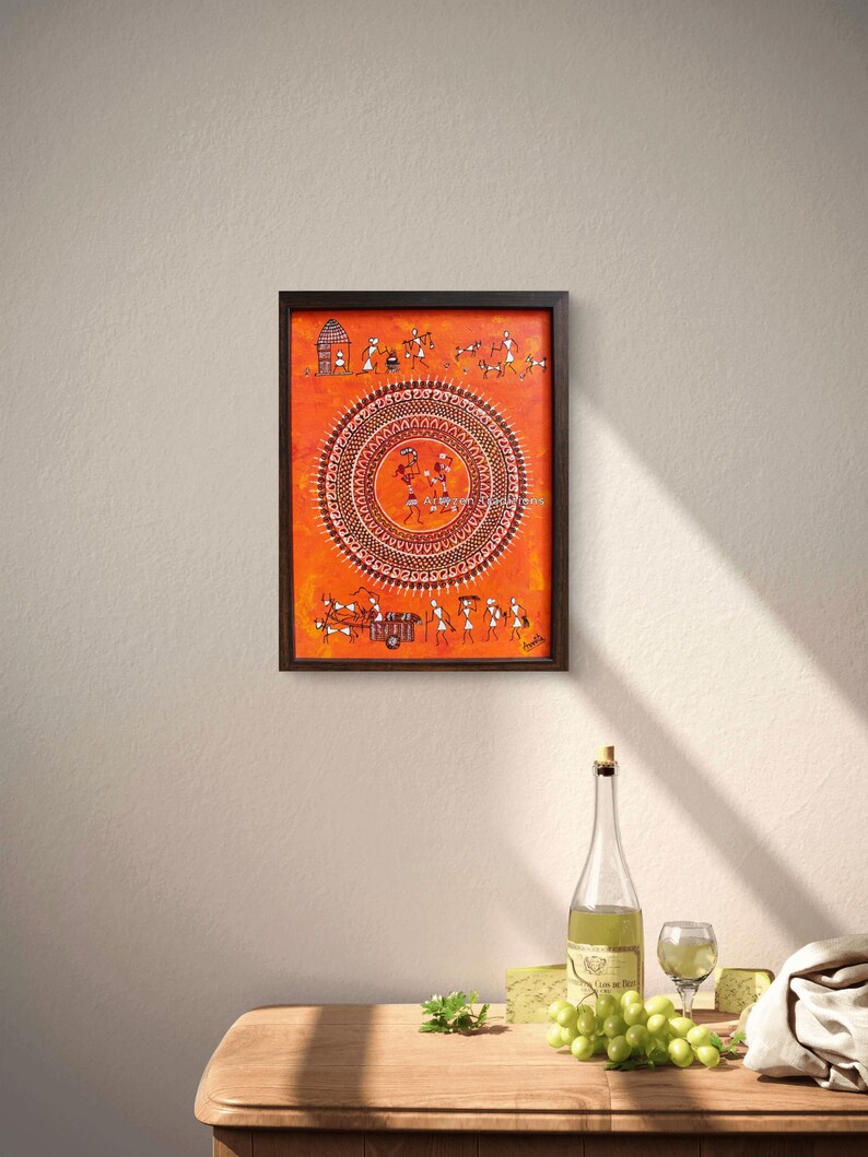 Pu&ograve; includere: Un dipinto rettangolare incorniciato su sfondo arancione con intricati disegni a linee bianche. L'opera mostra un grande motivo mandala circolare centrale circondato da piccole figure stilizzate, animali e scene di villaggio in stile tradizionale.