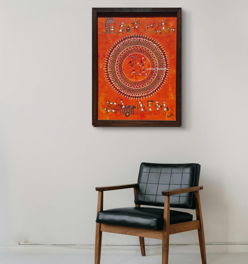 Pu&ograve; includere: Un'opera d'arte murale rettangolare in una cornice marrone scuro con uno sfondo arancione vibrante e intricate figure tribali bianche in stile Warli. Il design centrale &egrave; un grande motivo a mandala circolare con figure danzanti.