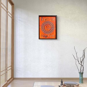 Pu&ograve; includere: Un'opera d'arte murale rettangolare caratterizzata da uno sfondo arancione vibrante con intricati motivi in bianco e nero in stile tribale. L'opera mostra un grande motivo circolare centrale circondato da piccole figure e strutture in una cornice scura.