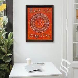 Pu&ograve; includere: Un dipinto rettangolare incorniciato su sfondo arancione con intricate figure bianche in stile Warli disposte in un grande motivo a mandala circolare centrale, con ulteriori piccole scene di persone e animali raffigurate sui bordi superiore e inferiore.