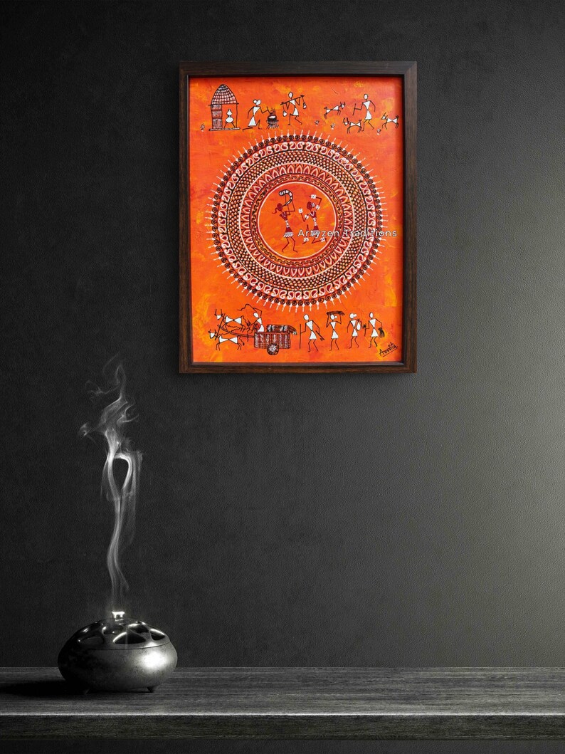 Pu&ograve; includere: Un dipinto rettangolare incorniciato che presenta figure stilizzate bianche in stile Warli su uno sfondo arancione vibrante. L'opera mostra un grande motivo mandala circolare centrale con figure danzanti, circondato da scene di vita quotidiana.