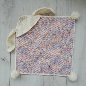 Peut inclure: Une couverture pour b&eacute;b&eacute; en tricot doux aux couleurs pastel avec un lapin en crochet blanc attach&eacute;. La couverture a un aspect textur&eacute; et duveteux et est parfaite pour une chambre de b&eacute;b&eacute;.