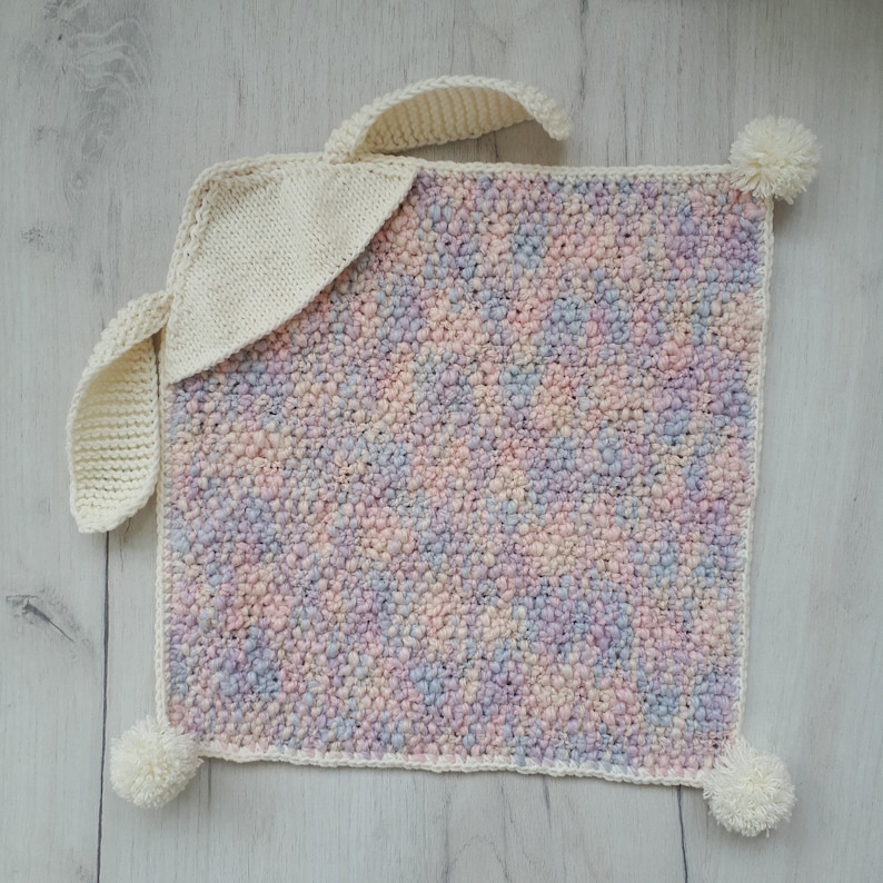 Peut inclure: Une couverture pour b&eacute;b&eacute; en tricot doux aux couleurs pastel avec un lapin en crochet blanc attach&eacute;. La couverture a un aspect textur&eacute; et duveteux et est parfaite pour une chambre de b&eacute;b&eacute;.