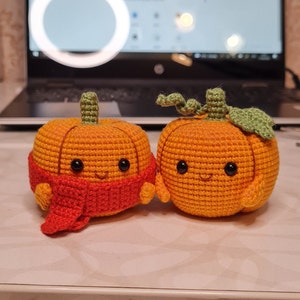 May include: Two crocheted pumpkins with smiling faces. One pumpkin is wearing a red scarf.