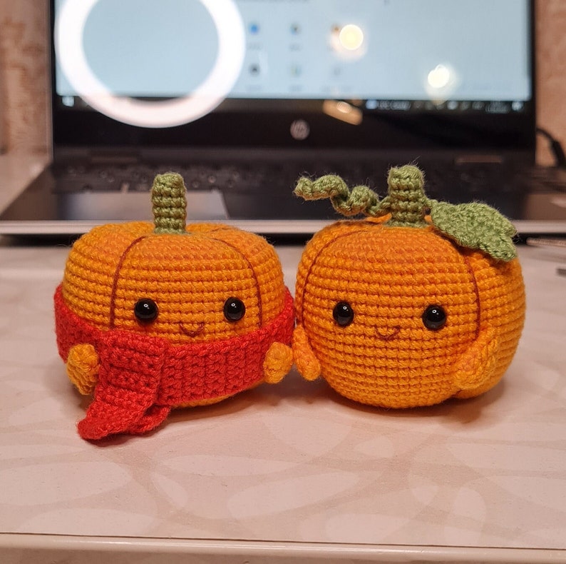 May include: Two crocheted pumpkins with smiling faces. One pumpkin is wearing a red scarf.