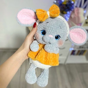 Peut inclure: Une souris en crochet grise avec des oreilles roses et un nœud jaune. La souris porte une robe jaune et a des yeux bleus.