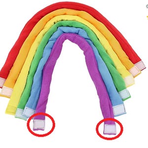 May include: A rainbow-shaped soft toy in red, orange, yellow, green, blue, and purple. The toy has a velvety texture and white velcro fastenings at the ends. This colourful toy is designed for children.