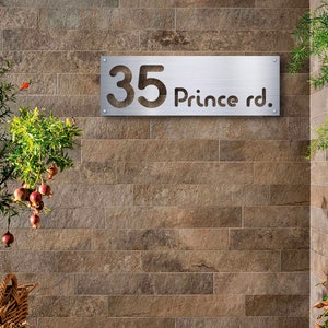 May include: A silver metal house number sign with the number 35 and the text "Prince rd." on a brown brick wall.
