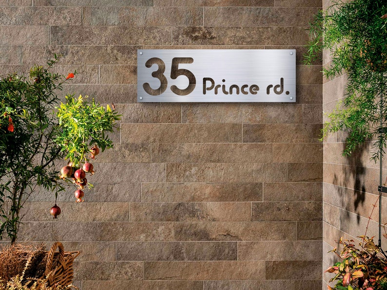 May include: A silver metal house number sign with the number 35 and the text "Prince rd." on a brown brick wall.
