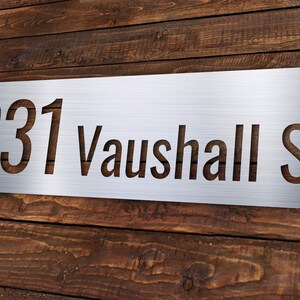 May include: A silver metal house number sign with the number 231 and the street name Vauxhall St cut out.