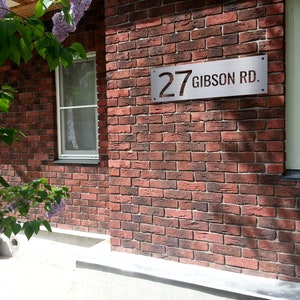 May include: A red brick house with a silver house number sign that reads "27 Gibson Rd."