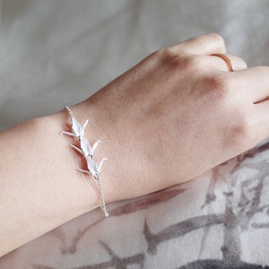 May include: A silver chain bracelet with three white origami cranes attached to it.