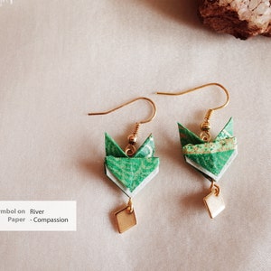 Pu&ograve; includere: Un paio di orecchini origami verdi con accenti dorati e un ciondolo quadrato. Gli orecchini sono realizzati in carta e hanno un design delicato e intricato. Il testo "Symbol on River Paper - Compassion" &egrave; visibile nell'immagine.