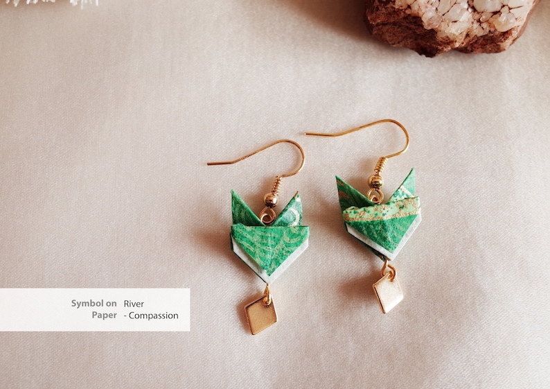 Pu&ograve; includere: Un paio di orecchini origami verdi con accenti dorati e un ciondolo quadrato. Gli orecchini sono realizzati in carta e hanno un design delicato e intricato. Il testo "Symbol on River Paper - Compassion" &egrave; visibile nell'immagine.