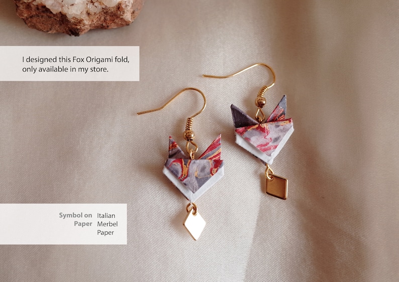 Pu&ograve; includere: Un paio di orecchini a forma di volpe origami dorati con un ciondolo a forma di diamante appeso a ciascuno. L'origami di volpe &egrave; realizzato con carta marmorizzata italiana con colori rosso, bianco e grigio.