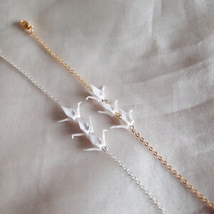 May include: Two delicate bracelets with origami paper crane charms. One bracelet has a silver chain and the other has a gold chain.