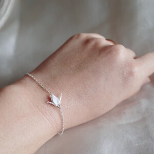May include: A silver chain bracelet with a white origami crane charm.